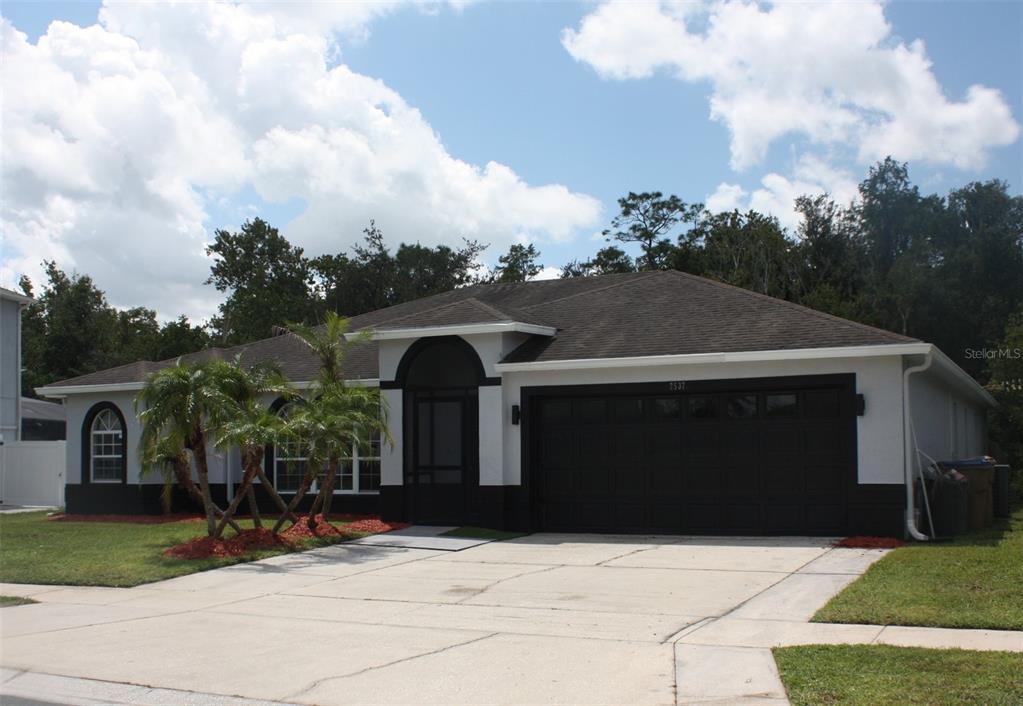 A single-story house with a white and black exterior, a two-car garage, and palm trees — 2537 JASMINE TRACE DRIVE, KISSIMMEE, FL
