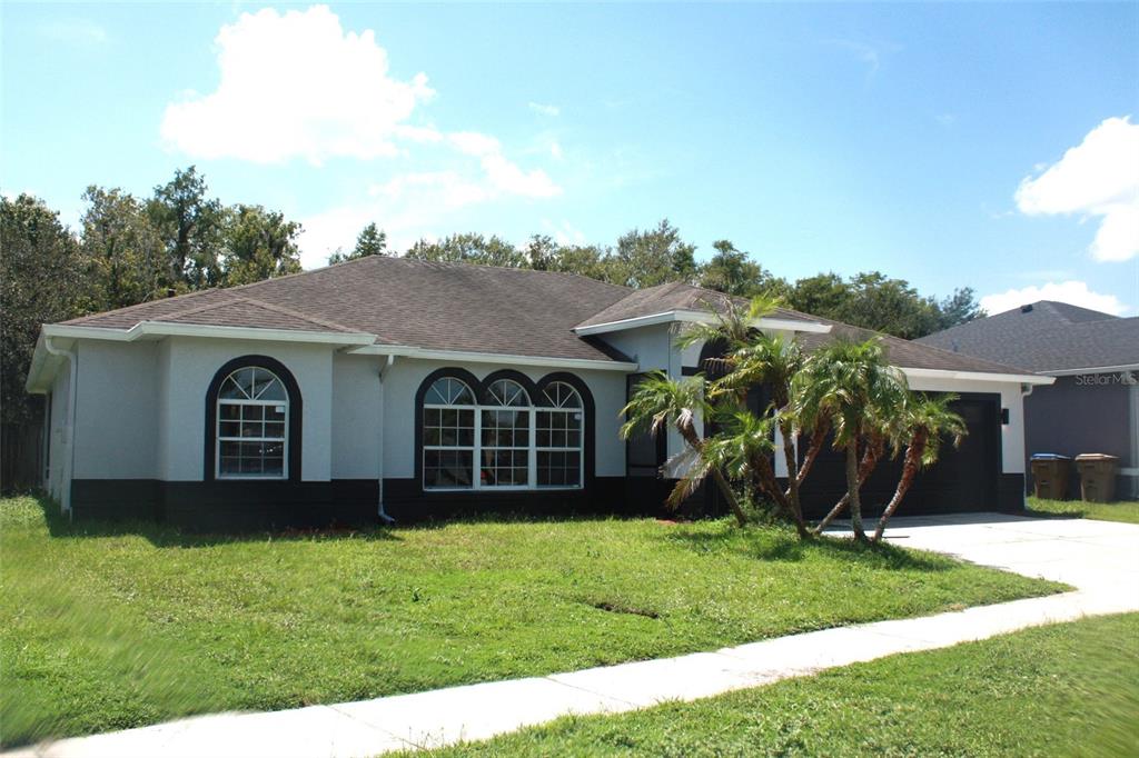 A single-story house with a gray exterior, dark trim, arched windows, and a palm tree — 2537 JASMINE TRACE DRIVE, KISSIMMEE, FL