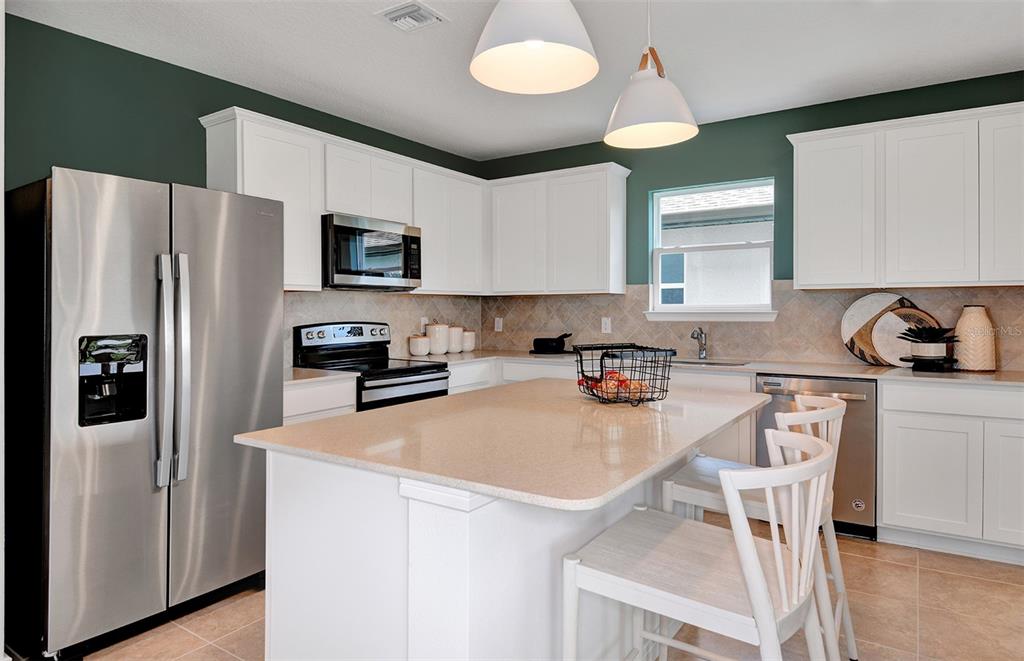 A kitchen features white cabinets, stainless steel appliances, a central island, and dark green walls — 10430 HIDDEN BANKS GLEN, PARRISH, FL