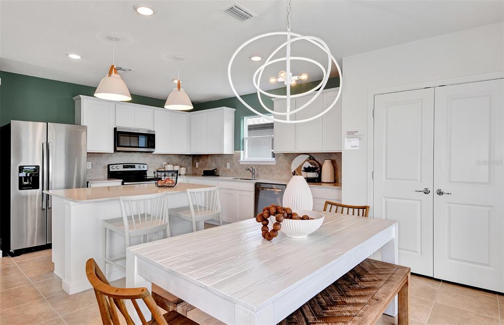 A kitchen with white cabinets, a central island, and a dining area with a wooden table — 10430 HIDDEN BANKS GLEN, PARRISH, FL