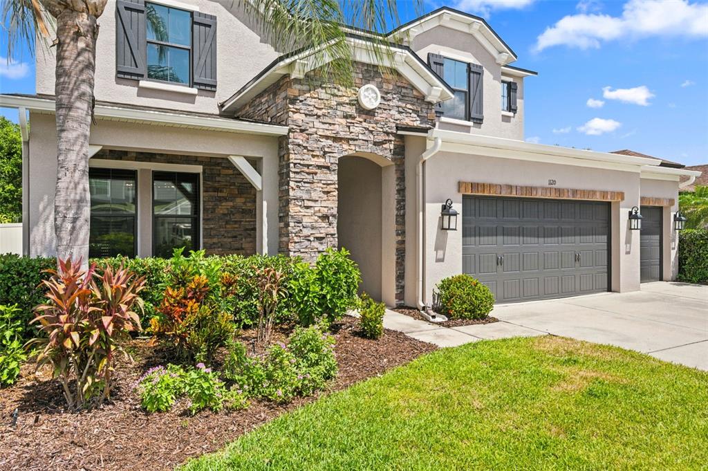 A two-story house with a stone facade, gray garage doors, and a landscaped front yard — 1120 MAZA PLACE, TRINITY, FL