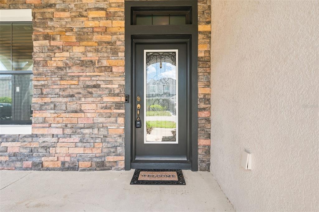 A dark front door with a glass insert sits between a stone wall and stucco — 1120 MAZA PLACE, TRINITY, FL