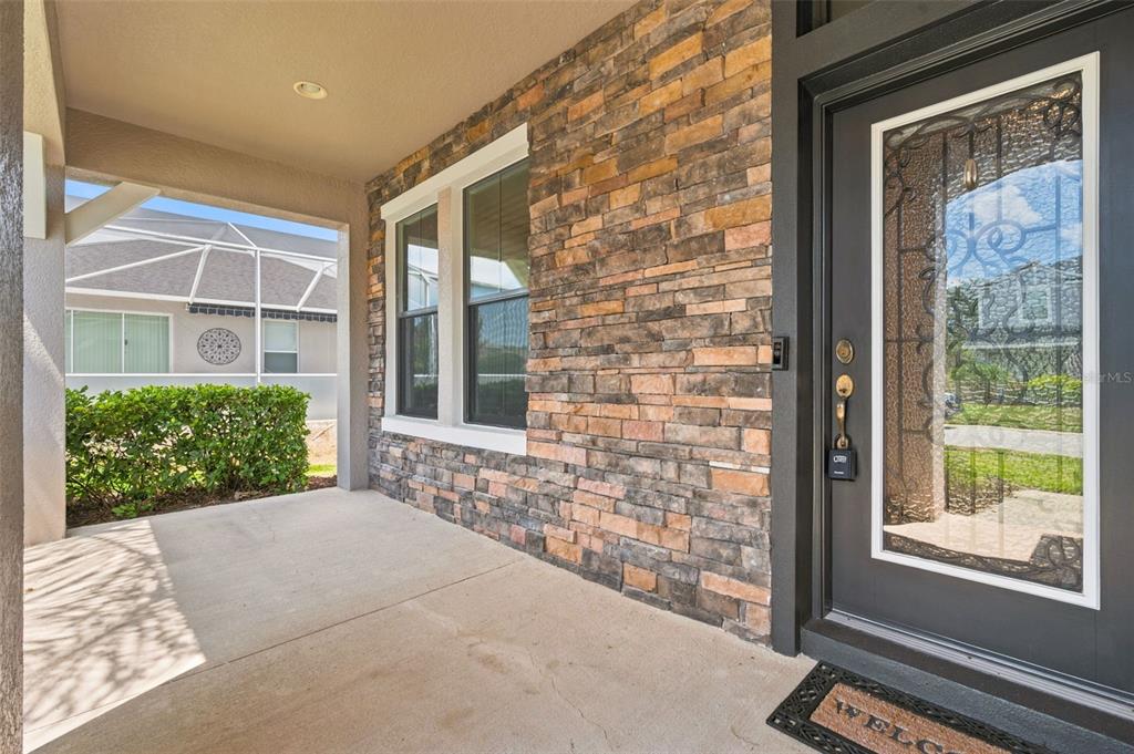 A covered front porch features a stone veneer wall, a dark door with glass, and windows — 1120 MAZA PLACE, TRINITY, FL