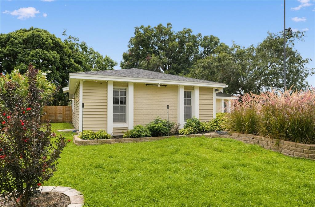 A tan, single-story detached building sits in a grassy backyard with a stone retaining wall — 312 HORMIGAS STREET, OCOEE, FL