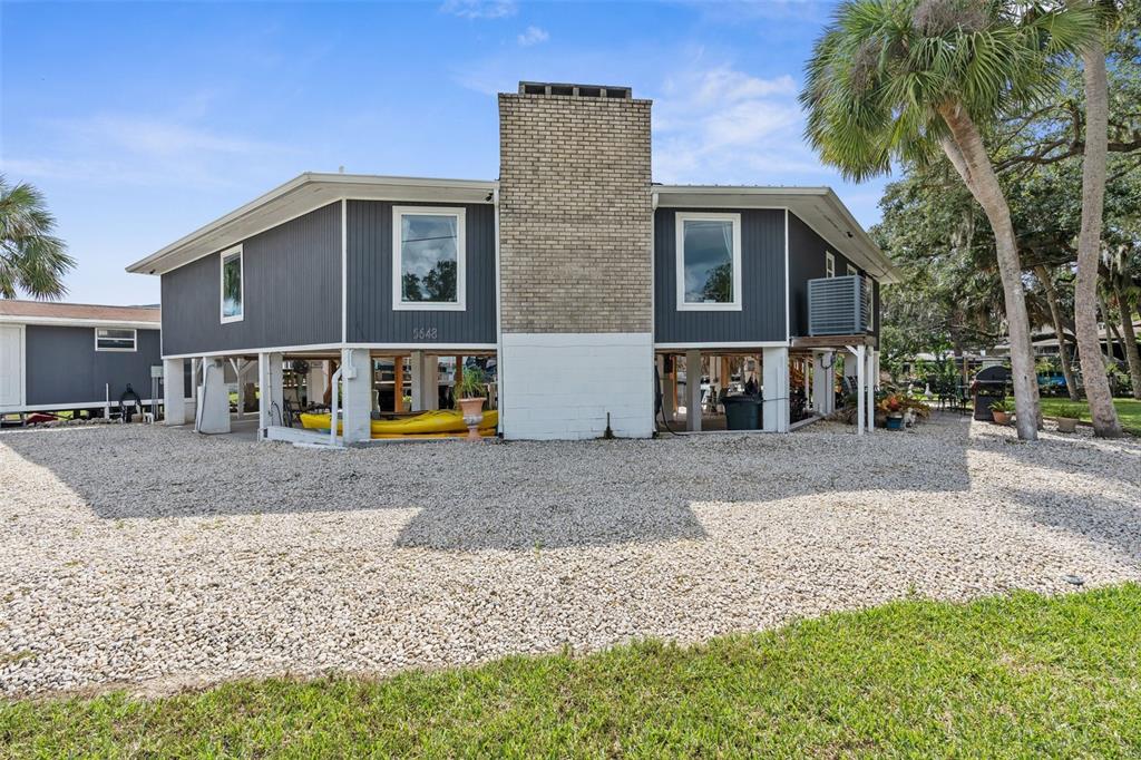 An elevated house with dark siding, a brick chimney, and a gravel yard at sunset — 5648 S GARCIA ROAD, HOMOSASSA, FL