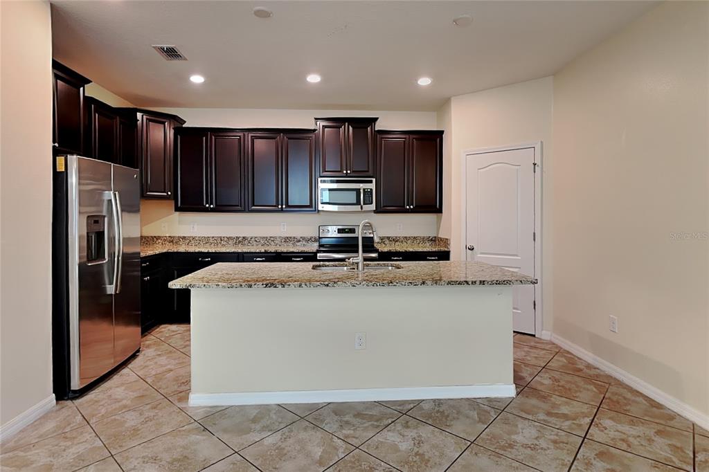 A kitchen features dark wood cabinets, granite countertops, a central island, and stainless steel appliances — 11020 WHITTNEY CHASE DRIVE, RIVERVIEW, FL