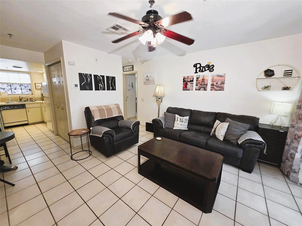 A living room features tile flooring, a dark sofa, a recliner, and Paris-themed wall decor — 2210 VISTA DEL SOL CIRCLE UNIT 502, LUTZ, FL