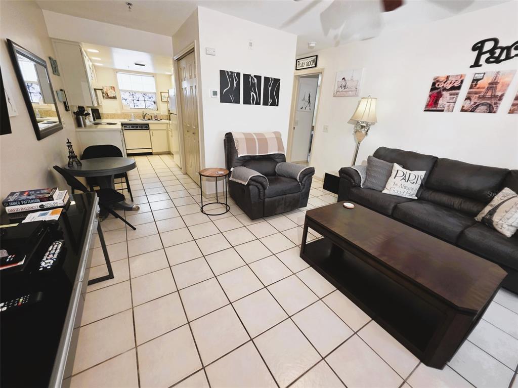 A living room with tile floors, a dark sofa, a recliner, and an adjacent kitchen area — 2210 VISTA DEL SOL CIRCLE UNIT 502, LUTZ, FL