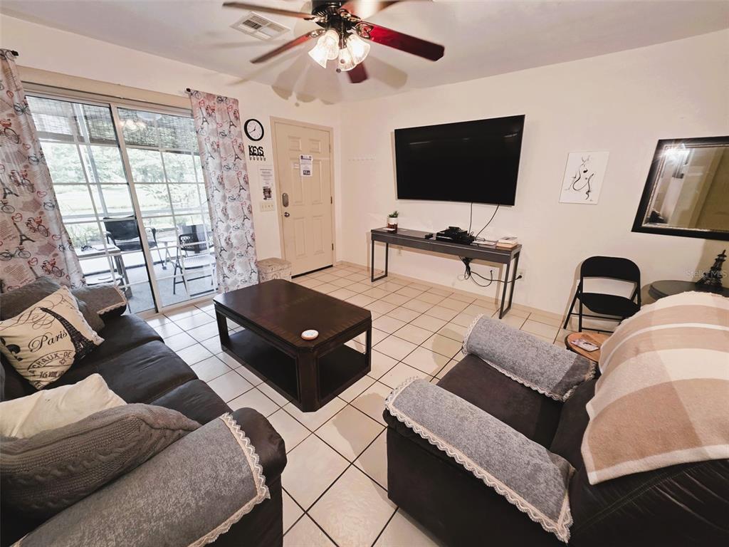 A living room features tile flooring, a ceiling fan, a television, and sliding glass doors — 2210 VISTA DEL SOL CIRCLE UNIT 502, LUTZ, FL