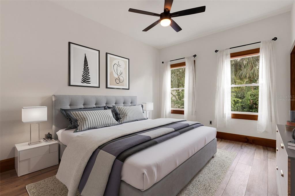 A bedroom features a gray upholstered bed, two windows with white curtains, and wood flooring — 711 E LIME STREET, LAKELAND, FL