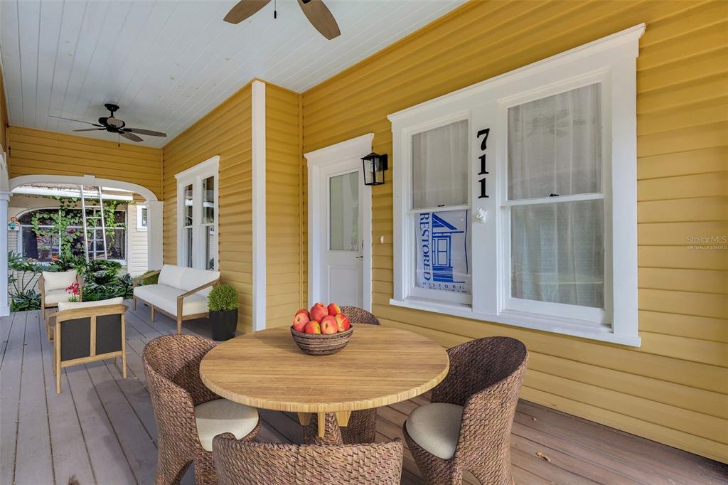 A covered porch features yellow siding, a round wooden table with wicker chairs, and seating — 711 E LIME STREET, LAKELAND, FL