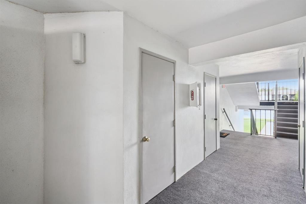 A carpeted apartment hallway features two gray doors, a fire extinguisher cabinet, and exterior stairs — 8215 SUN SPRING CIRCLE UNIT 12, ORLANDO, FL