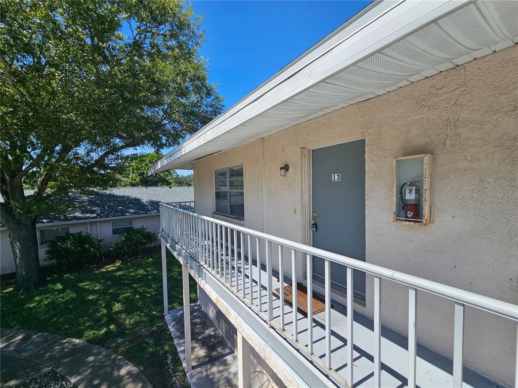 An exterior view of an apartment balcony with a gray door labeled 13 — 209 NW JEFFERSON CIRCLE N UNIT 13, ST PETERSBURG, FL