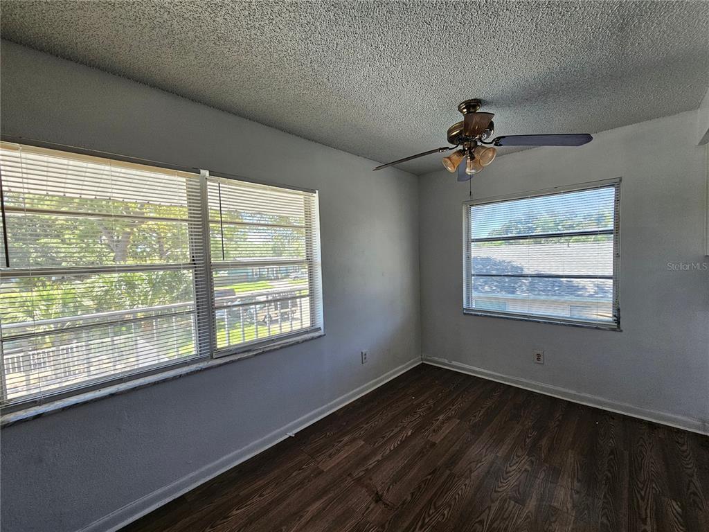An empty room features wood-look flooring, light gray walls, a ceiling fan, and two windows — 209 NW JEFFERSON CIRCLE N UNIT 13, ST PETERSBURG, FL