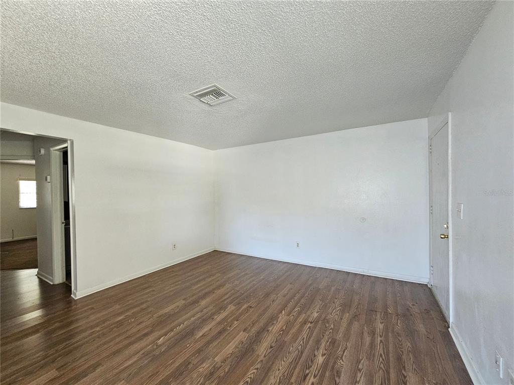 An empty room features white walls, a textured ceiling, and wood-look laminate flooring — 209 NW JEFFERSON CIRCLE N UNIT 13, ST PETERSBURG, FL