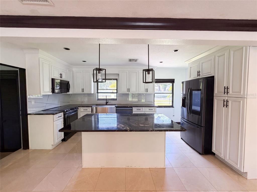 A kitchen features white cabinetry, black countertops, a central island, and black stainless steel appliances — 1515 S WEST SHORE BOULEVARD, TAMPA, FL