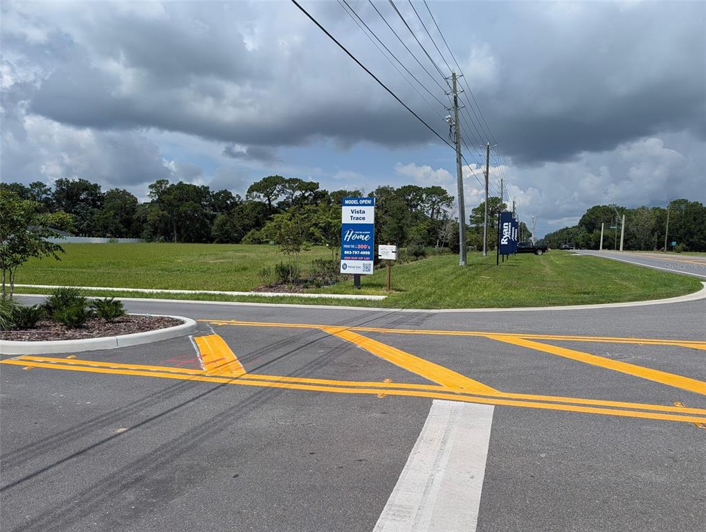 A grassy vacant lot with a real estate sign stands at a road intersection — EAST HWY 25, BELLEVIEW, FL