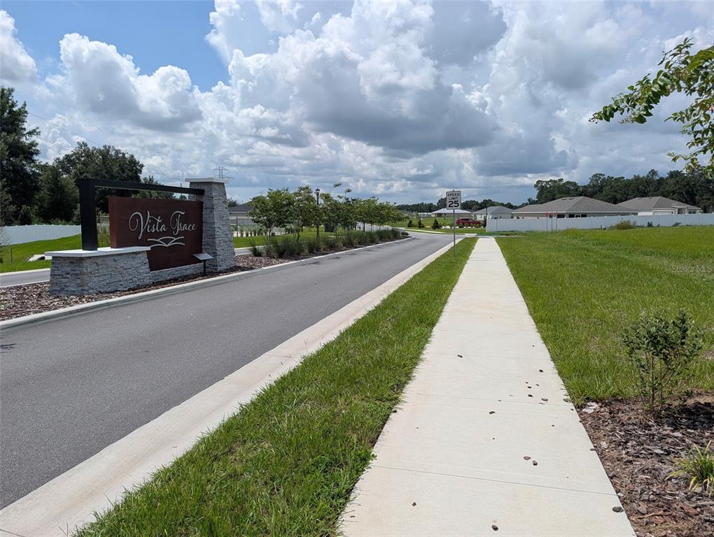 A stone and metal monument sign marks the entrance to a residential neighborhood with sidewalks — EAST HWY 25, BELLEVIEW, FL