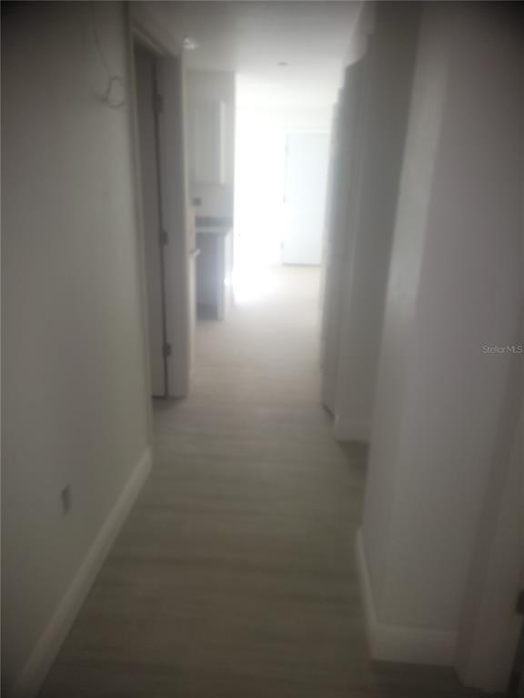 A hallway with light-colored flooring leads toward a bright doorway in the distance — 338 2ND WAY, INTERLACHEN, FL