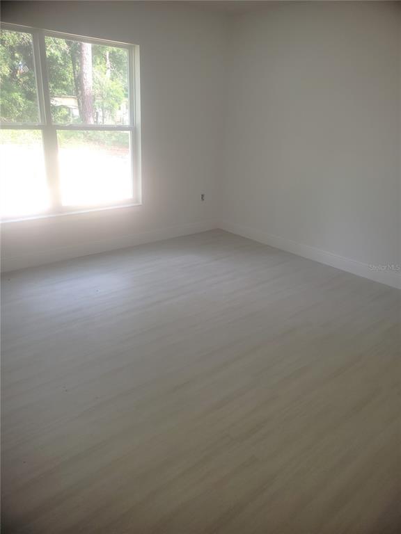 An empty room features light-colored wood-look flooring, white walls, and a large window — 338 2ND WAY, INTERLACHEN, FL