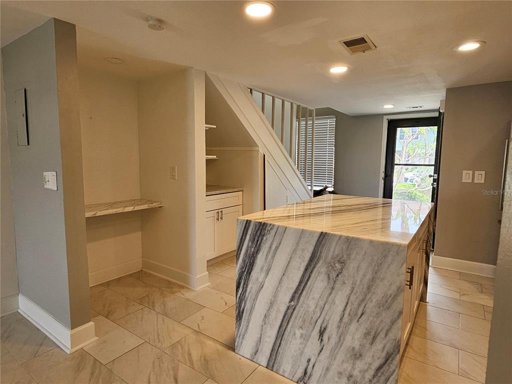 A kitchen features a large marble-topped island, tile flooring, and built-in shelving under a staircase — 1028 APOLLO BEACH BOULEVARD UNIT 19, APOLLO BEACH, FL