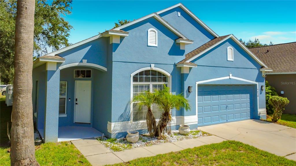 A blue single-story house with a white-trimmed front door, arched window, and two-car garage — 9850 HIDDEN DUNES LANE, ORLANDO, FL