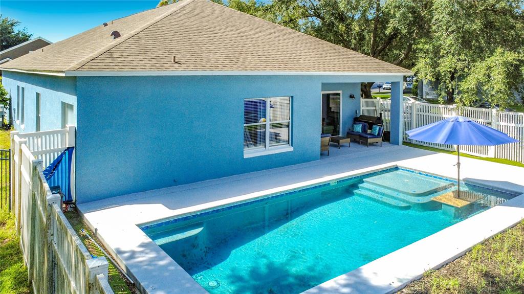 A blue house features a backyard swimming pool with a built-in table and blue umbrella — 9850 HIDDEN DUNES LANE, ORLANDO, FL