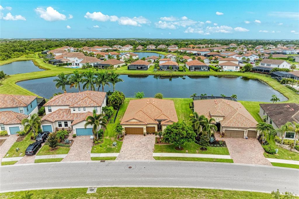 An aerial view shows three suburban houses with tile roofs situated along a lake — 3512 SAVANNA PALMS COURT, LAKEWOOD RANCH, FL