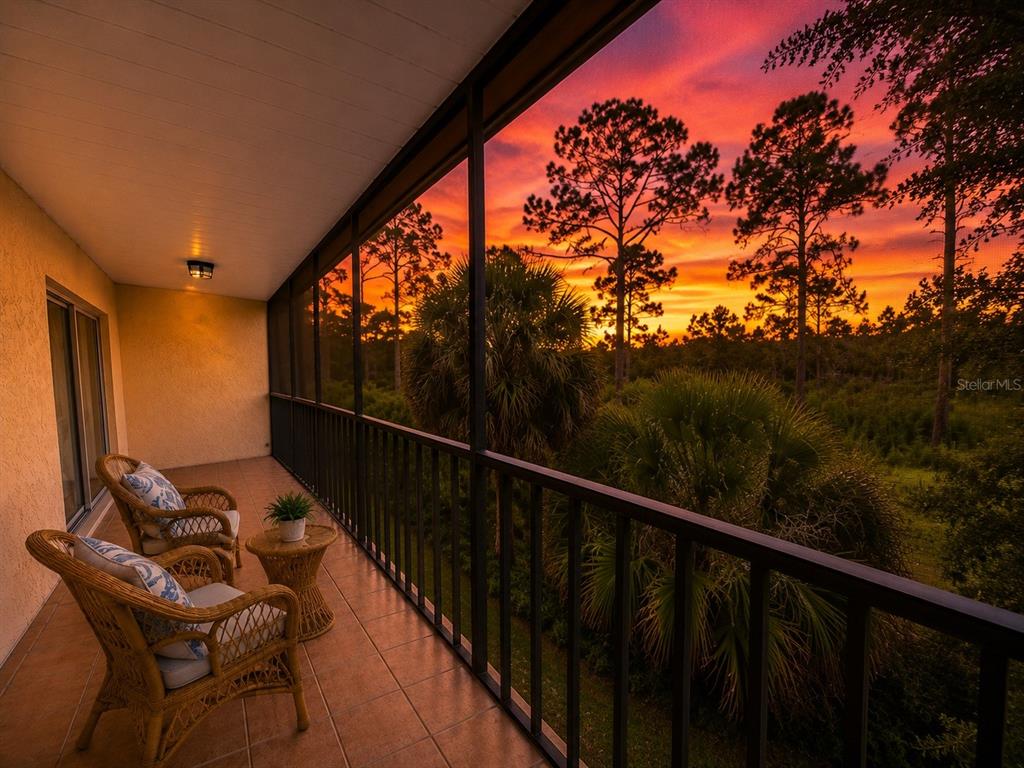 A screened-in balcony with wicker chairs and tile flooring overlooks a sunset over trees — 211 RUBENS DRIVE UNIT E, NOKOMIS, FL