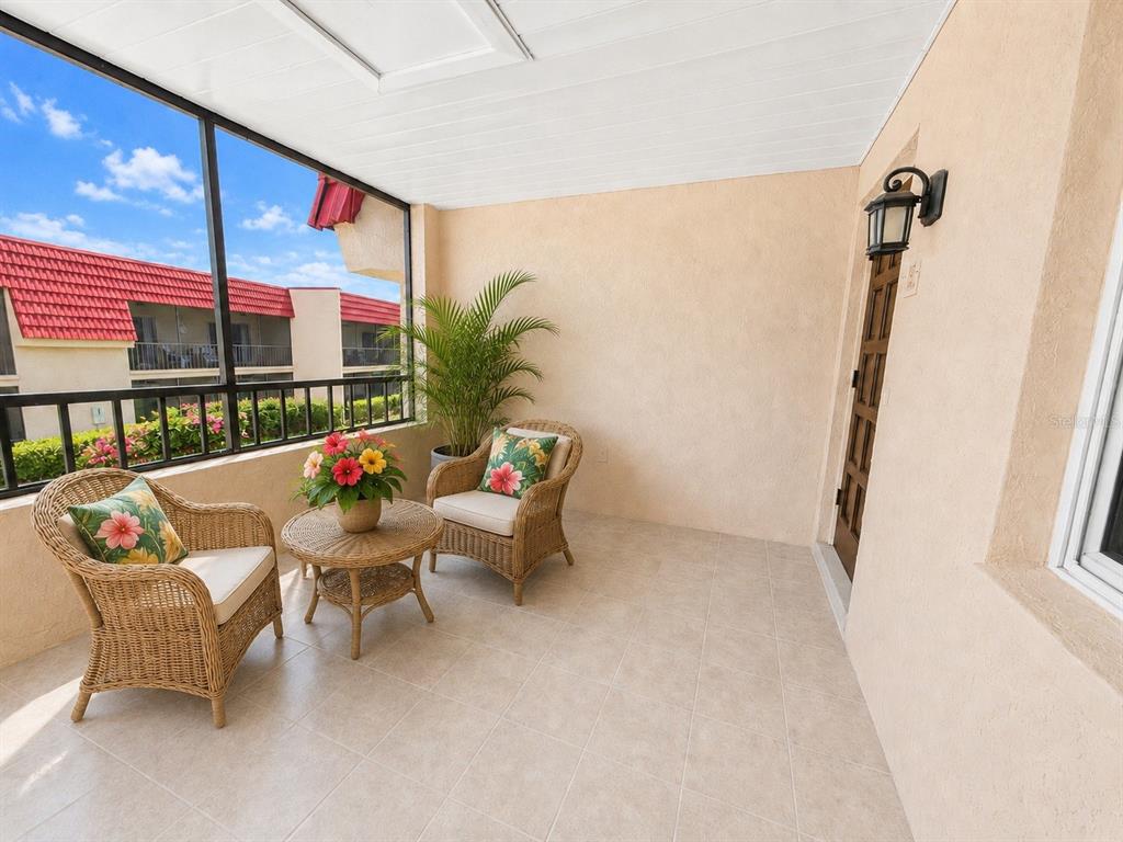 A screened-in balcony features wicker furniture, a potted plant, and tiled flooring — 211 RUBENS DRIVE UNIT E, NOKOMIS, FL