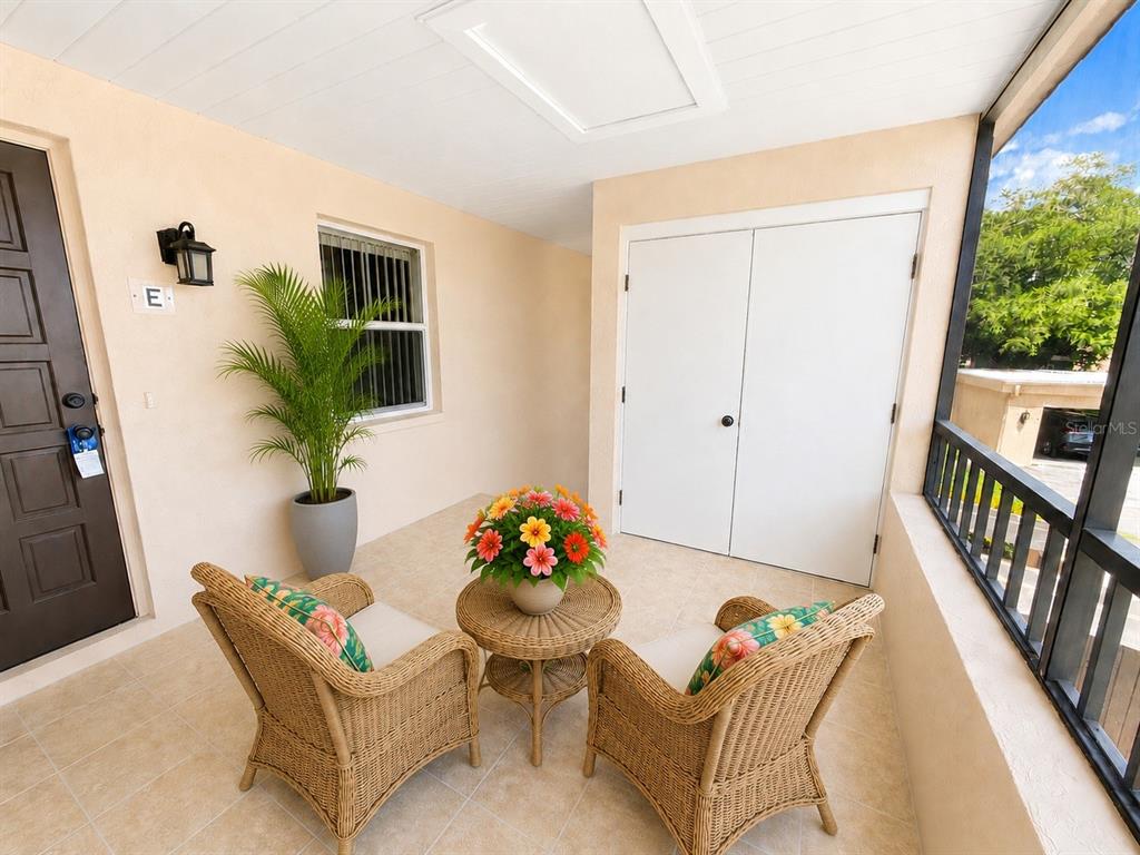 A covered patio features two wicker chairs, a small table, a potted plant, and double doors — 211 RUBENS DRIVE UNIT E, NOKOMIS, FL