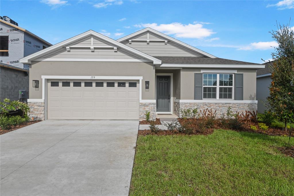A single-story suburban house features a two-car garage, stone veneer accents, and gray siding — 159 WATERSTONE LOOP, TAVARES, FL