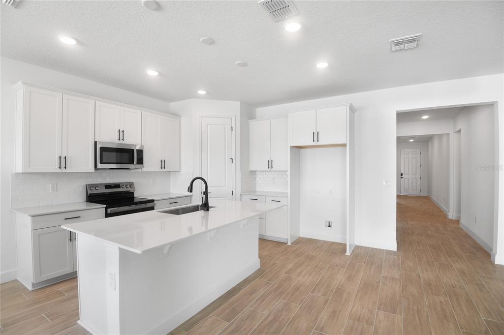 A modern kitchen features white cabinetry, a central island with a sink, and stainless appliances — 159 WATERSTONE LOOP, TAVARES, FL