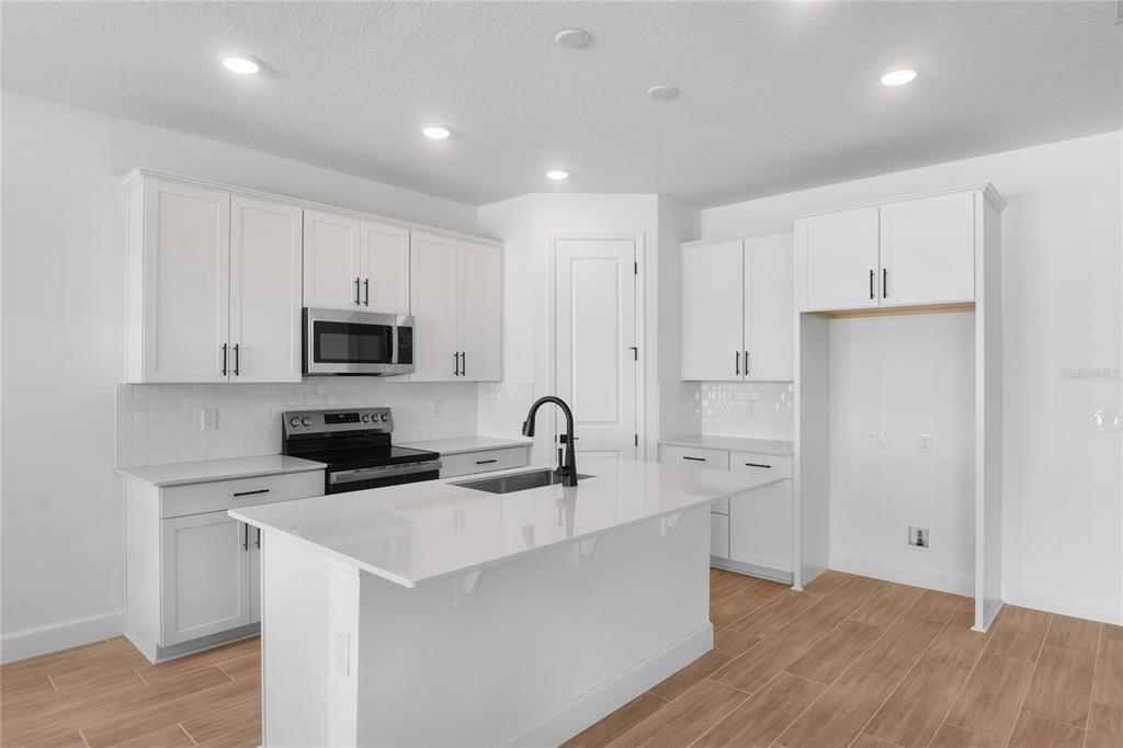 A kitchen features white cabinets, a stainless steel microwave, a glass-top stove, and subway tile — 159 WATERSTONE LOOP, TAVARES, FL