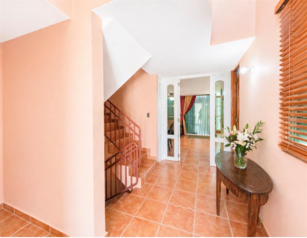 An entryway with terracotta tile floors, a staircase with metal railings, and a wooden console table — The Village at the Hill FLAMENCO UNIT 50, CEIBA, PR