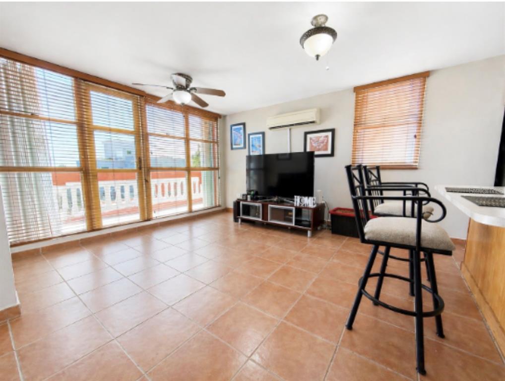 A living room with tile floors, a ceiling fan, a television, and large windows — The Village at the Hill FLAMENCO UNIT 50, CEIBA, PR