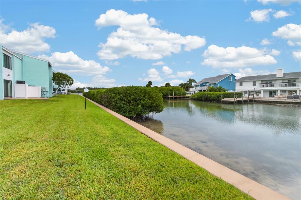 A grassy lawn borders a canal with mangroves and houses in the background — 1 WINDRUSH BOULEVARD UNIT 65, INDIAN ROCKS BEACH, FL