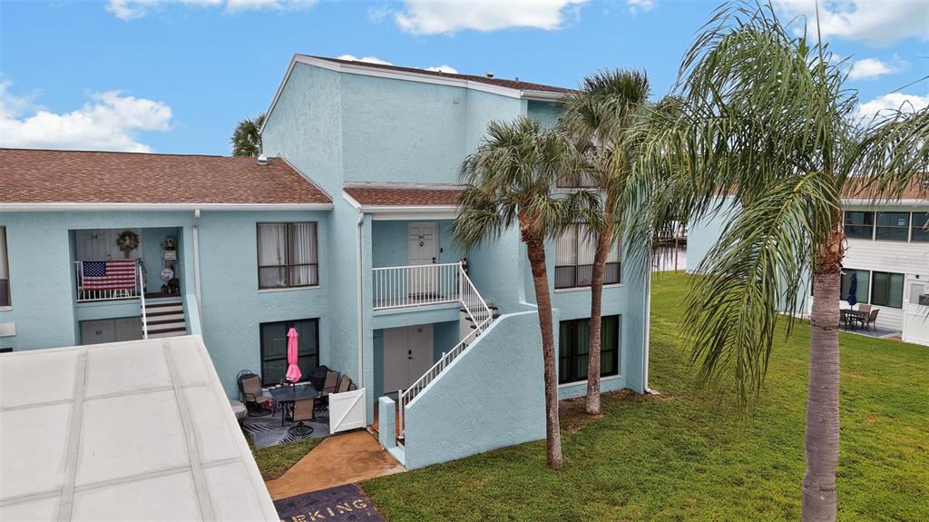 An exterior view of a light blue two-story apartment building with palm trees and grass — 1 WINDRUSH BOULEVARD UNIT 65, INDIAN ROCKS BEACH, FL
