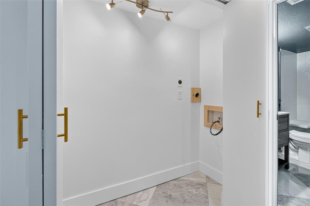 A small laundry area features marble-patterned tile flooring, gold hardware, and wall-mounted utility connections — 1 WINDRUSH BOULEVARD UNIT 65, INDIAN ROCKS BEACH, FL