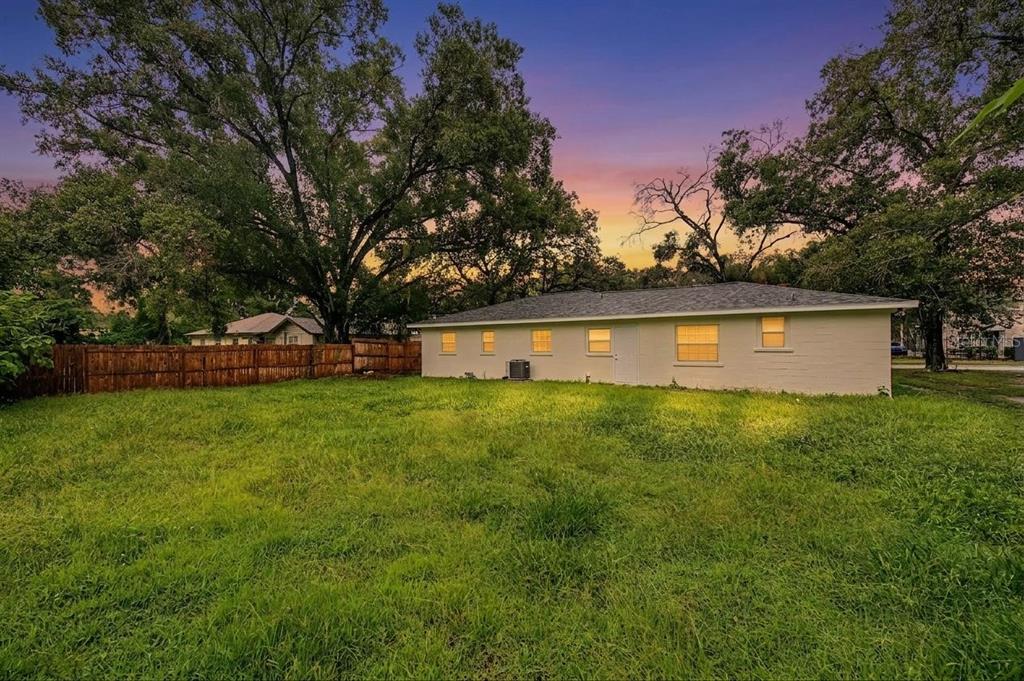 The exterior of a light-colored house with a large backyard and mature trees at sunset — 810 E 120TH AVENUE, TAMPA, FL