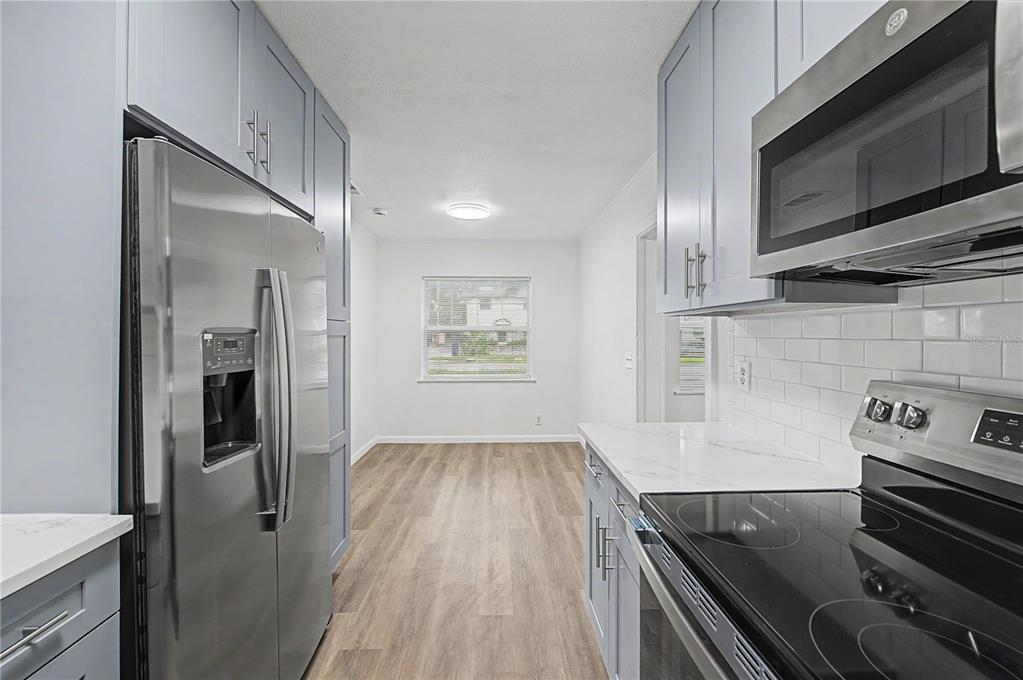 A galley kitchen features light blue cabinets, stainless steel appliances, and wood-look flooring — 810 E 120TH AVENUE, TAMPA, FL