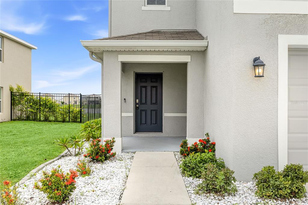 A concrete walkway leads to the dark front door of a gray stucco house — 10116 CHARLOTTE DRIVE, PARRISH, FL
