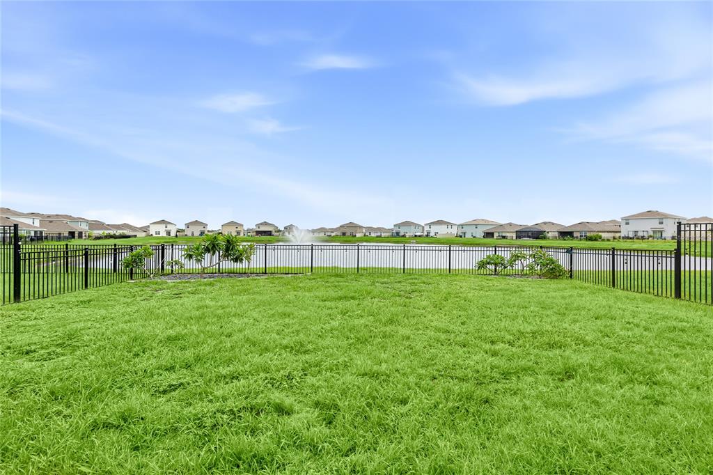 A grassy backyard features a black metal fence overlooking a pond with a fountain — 10116 CHARLOTTE DRIVE, PARRISH, FL