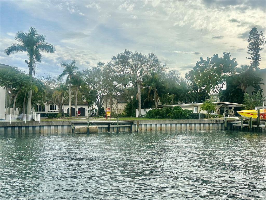 A vacant waterfront lot features a seawall, mature trees, and a for sale sign — 52 SANDPIPER ROAD, TAMPA, FL