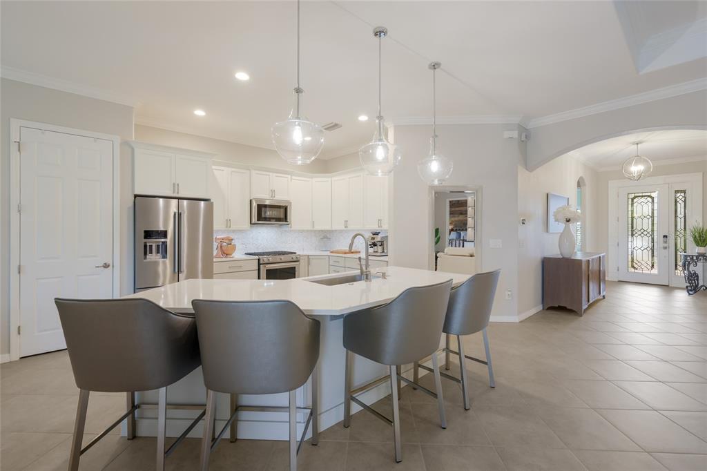 A kitchen features a white island with gray stools, stainless steel appliances, and pendant lighting — 13017 RAMBLEWOOD TRAIL, BRADENTON, FL