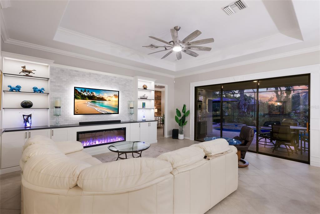 A living room features a white sectional sofa, a fireplace, built-in shelving, and sliding glass doors — 13017 RAMBLEWOOD TRAIL, BRADENTON, FL