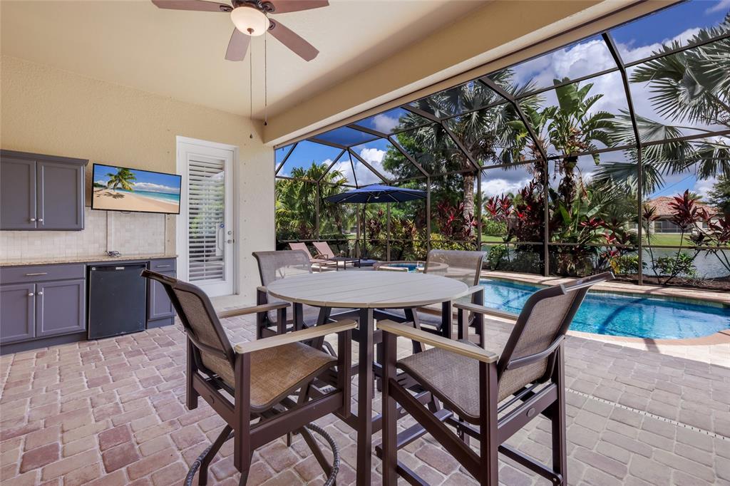 A covered patio features a dining set, outdoor kitchen, and a screened-in pool area — 13017 RAMBLEWOOD TRAIL, BRADENTON, FL
