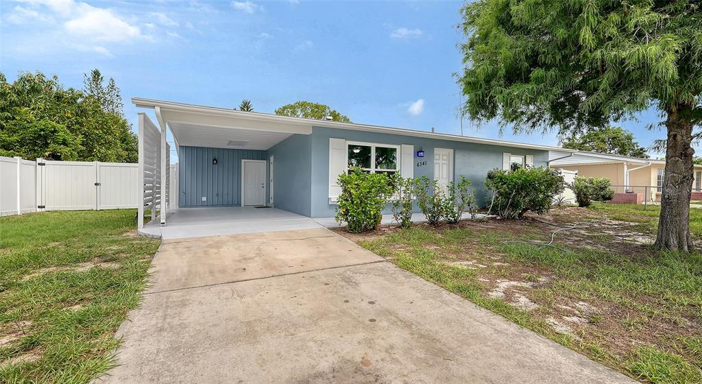 A single-story blue house features a concrete driveway, a carport, and a white privacy fence — 4341 GORGAS, NORTH PORT, FL