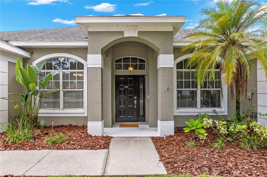 The exterior of a single-story home features a covered entryway, a dark door, and landscaping — 1604 LORIANA STREET, BRANDON, FL