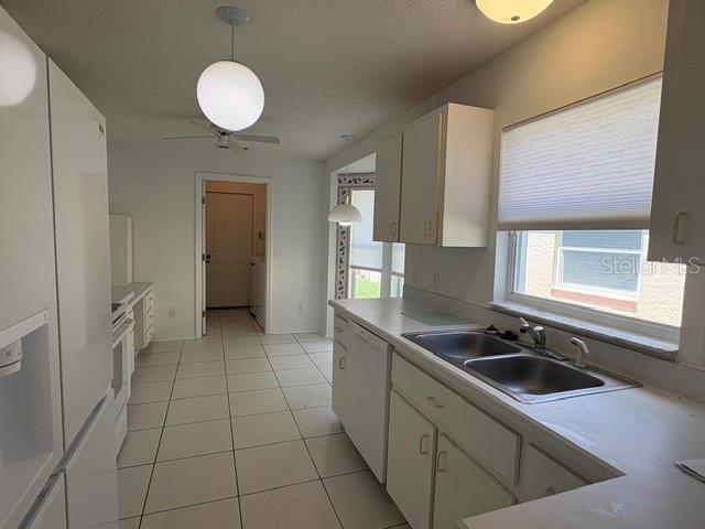 A kitchen with white cabinets, white appliances, tiled floors, and a double sink under a window — 505 CEDAREDGE DRIVE, NEW SMYRNA BEACH, FL